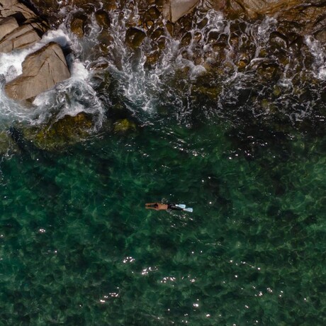 Aerial view of a snorkeller in clear turquoise waters near rocky coastline at Amanpuri, Thailand.