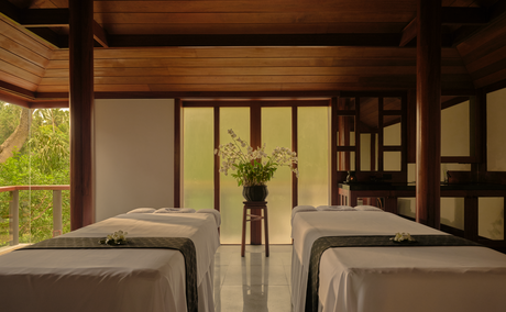 Salle de traitement double à Amanpuri, station thermale avec deux lits de massage et baies vitrées donnant sur la nature.