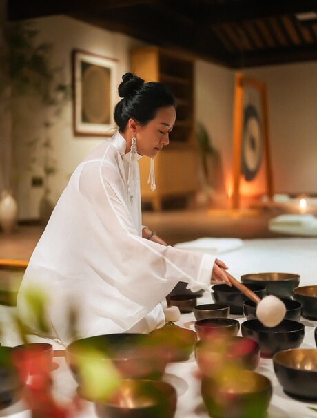 Woman in white shirt preparing tea at Amanfayun, with traditional pottery and candles on table.