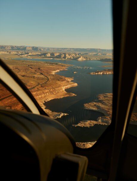 Aerial view of Lake Powell from a private aircraft, showing terracotta-hued landscape meeting blue water near Amangiri.