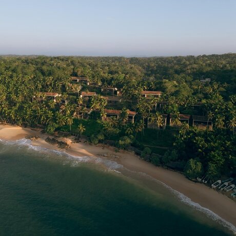 Aerial view of Amanwella's beachfront suites set amongst dense tropical forest along a quiet sandy cove.