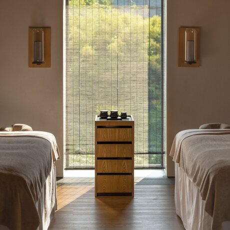 Spa treatment room at Amanyangyun with two massage beds facing a large window and central wooden cabinet.
