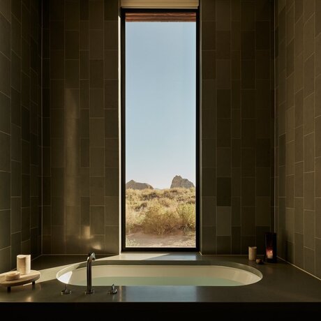 Amangiri suite bathtub with framed desert landscape view through tall window.