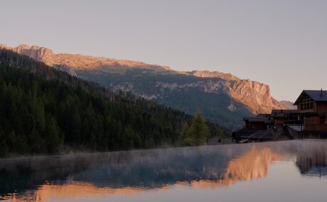 Outdoor pool reflecting Alpine mountains at sunrise, Aman Rosa Alpina resort.