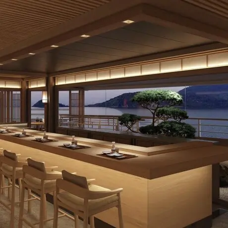 Dining venue at Aman with floor-to-ceiling windows overlooking twilight waters and coastline.
