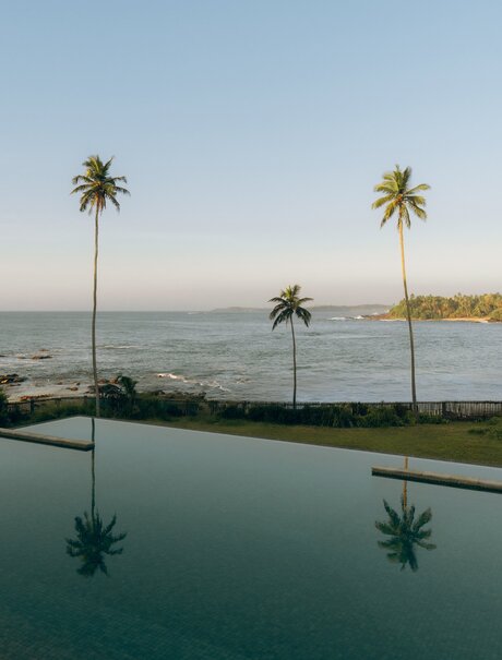 Infinity pool overlooking the Indian Ocean at Amanwella, Sri Lanka, with palm trees reflected in still water.