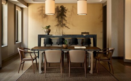 Dining area in an Aman Suite at Aman New York, featuring a wooden table with chairs and pendant lighting.
