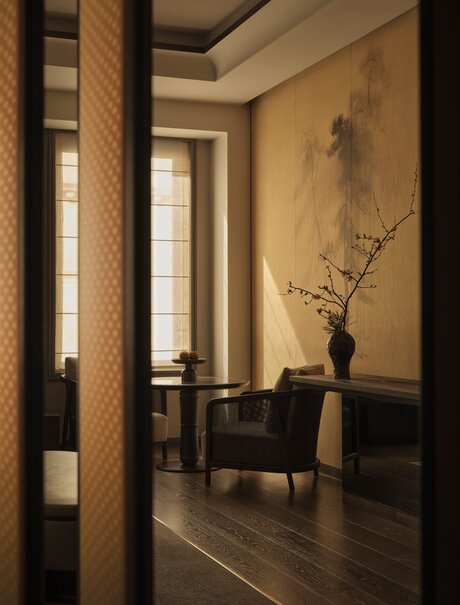Premier Suite entrance at Aman New York, featuring a dark wood floor, cream walls, and minimalist decor with a solitary vase.
