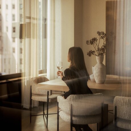 Penthouse PH24 three-bedroom home in New York with guest seated at desk by tall windows.