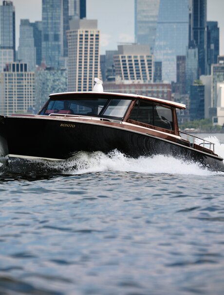 Sleek black speedboat cutting through Hudson River waters with Manhattan skyline behind, Aman New York.