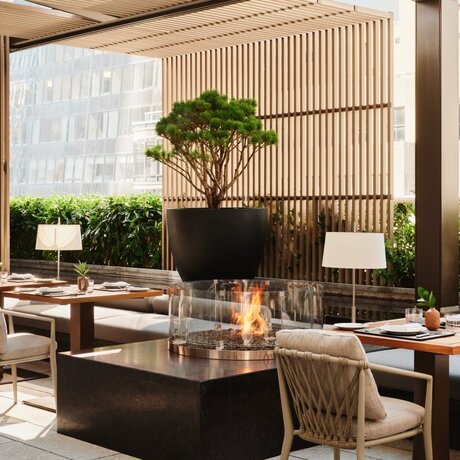 Arva Garden Terrace dining room at Aman New York, with tables, chairs, and a sculptural tree centrepiece.