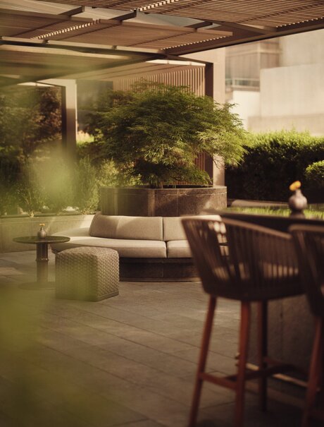 Rooftop terrace at Aman New York with seating area and greenery at dusk.