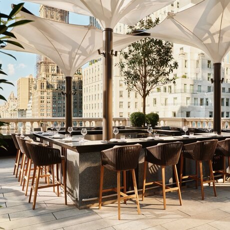 Garden terrace bar at Aman New York with wooden seating and city views.
