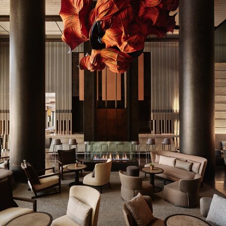 Aman New York's lounge interior with soaring columns, contemporary seating arrangements, and a striking amber-toned sculptural installation overhead.
