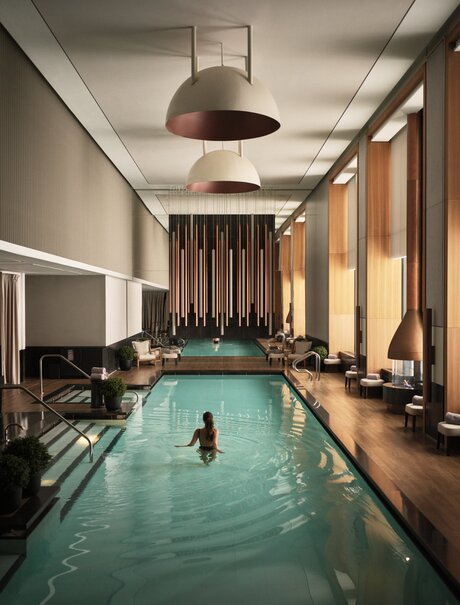 Swimming pool at Aman New York with warm lighting and floor-to-ceiling windows.