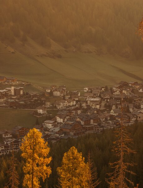 Veduta autunnale della valle di San Cassiano dal resort Aman Rosa Alpina, con larici dorati in primo piano.