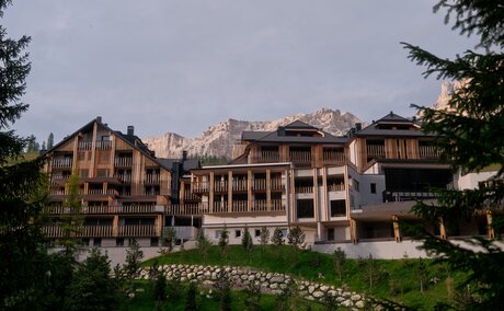 Aman Rosa Alpina resort exterior at dusk, framed by alpine vegetation.