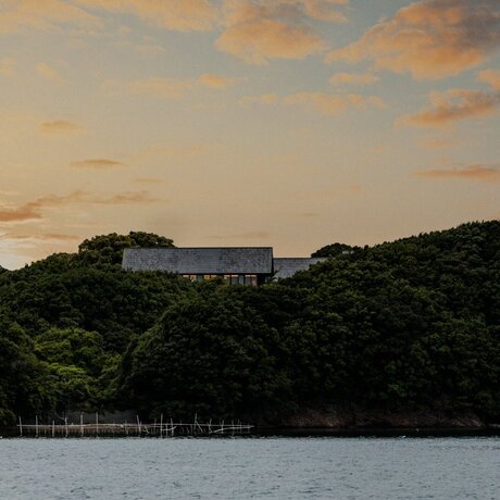Amanemu resort perched on forested hillside at sunset overlooking calm waters, Japan.