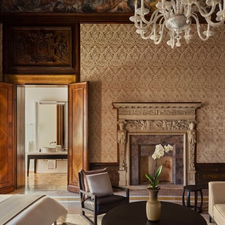 Sansovino Stanza bedroom at Aman Venice, with ornate fireplace, wooden doors, and period furniture.