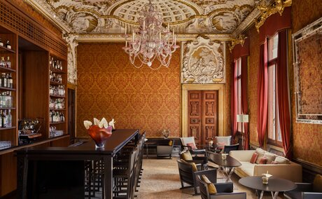 Bar at Aman Venice with warm ochre walls, ornate ceiling, and elegant seating areas in Venice, Italy.