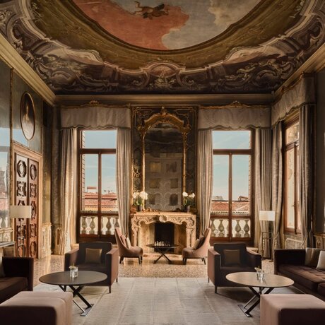Tiepolo Room at Aman Venice, with frescoed ceiling, marble fireplace, and tall windows overlooking the Grand Canal.