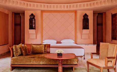 Amanjena pavilion principal bedroom with terracotta walls, carved wooden doors, and traditional Moroccan furnishings.