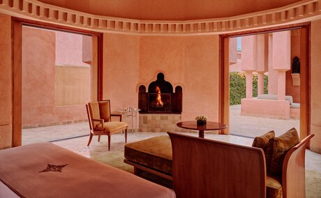 Pavilion 36 bedroom at Amanjena in Morocco, featuring terracotta walls, wooden furniture and arched windows.