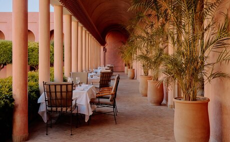 Terracotta columns frame a shaded corridor at Amanjena, with traditional seating and climbing ivy along the walls.