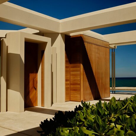 Beachfront casita with wooden doors and cream walls beneath a blue sky at Amanvari, Mexico.