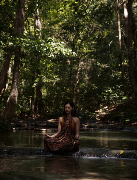 Woman meditating in river at Amanwana, Indonesia, surrounded by forest canopy.