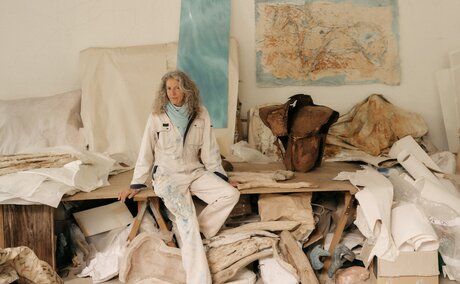 Studio portrait of Alexandra Athanasiades at Amanzoe, Greece, seated among scattered papers and materials.