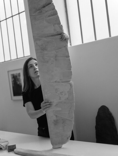 Studio portrait of artist Despina Flessa with large stone sculpture at Amanzoe, Greece.