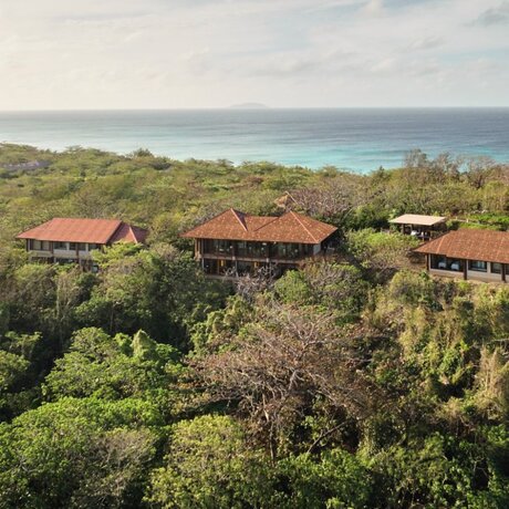Aerial view of Aman Spa nestled amongst tropical vegetation at Amanpulo, Philippines, with turquoise waters visible beyond.