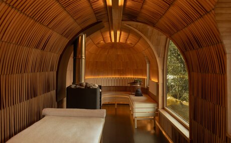 Wooden sauna interior at Amankora's Paro Lodge, with bench seating and large window overlooking the landscape.