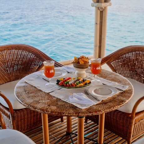 Floating bar table at Amanpulo resort with woven chairs, fresh fruit and cocktails overlooking turquoise waters, Philippines.