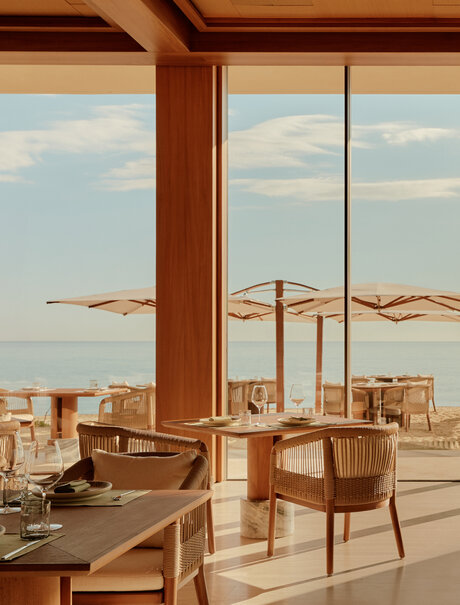 Amanvari interior lounge with wooden furniture and expansive city views through floor-to-ceiling windows.