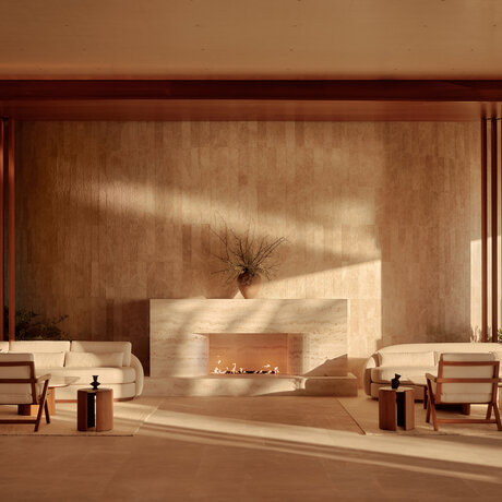 Amanvari's minimalist lounge with travertine fireplace and warm earth-toned walls.