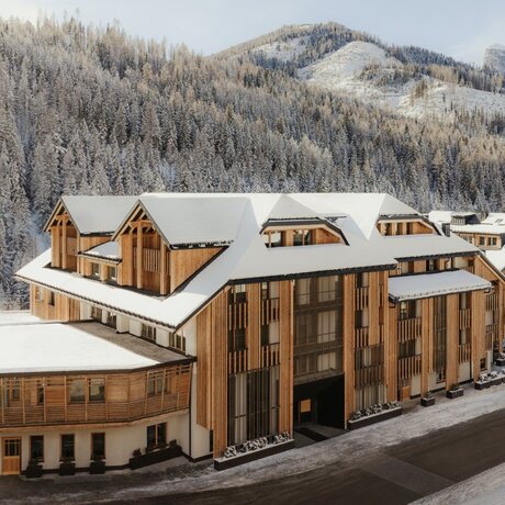 Aman Rosa Alpina exterior with snow-covered Alpine peaks and forested slopes in the background.