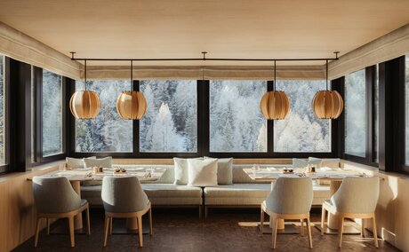 The Heritage Room at Aman Rosa Alpina features floor-to-ceiling windows overlooking Alpine peaks, with contemporary artwork and warm wooden furnishings.