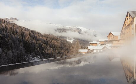 Outdoor pool at Aman Rosa Alpina overlooking snow-capped Italian Alps and misty lakeside landscape.