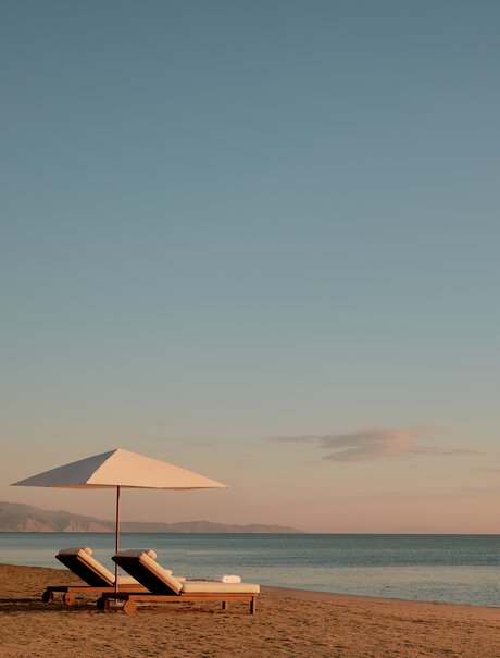 Two sun loungers and parasol on Amanvari's beach at sunset.
