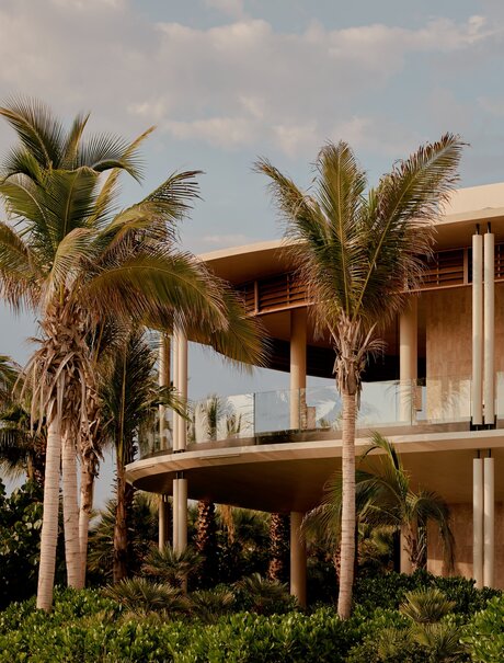 Casa Grande at Amanvari, a two-storey wooden residence with palm trees, set against a cloudy sky in Mexico.