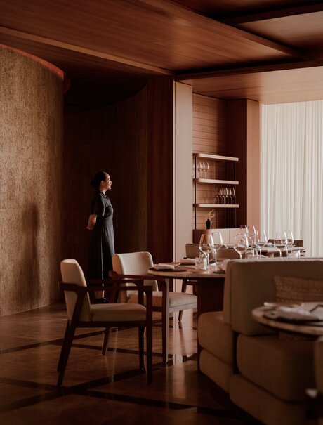 Warm-toned study at Amanvari with wooden furniture, shelving, and desk by soft lighting.