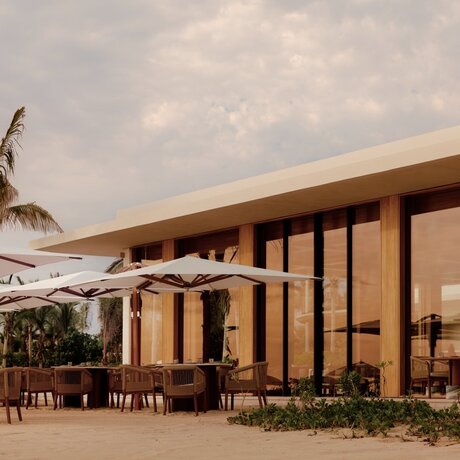 Amanvari villa with wooden facade and terrace overlooking tropical landscape at sunset.