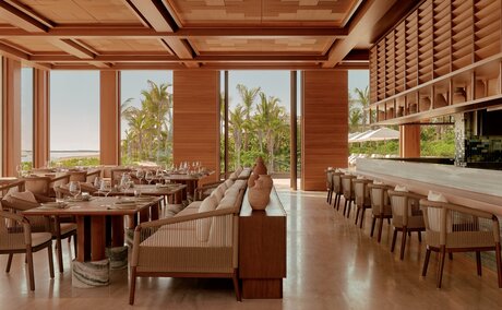 Amanvari dining venue with wooden interiors, floor-to-ceiling windows overlooking Mexican landscape, and contemporary furnishings.