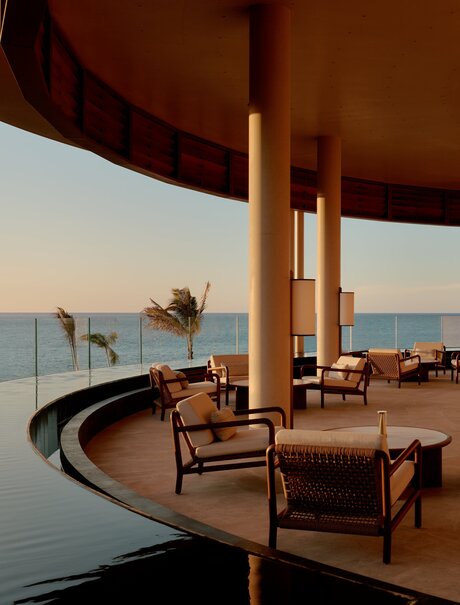 Amanvari's lounge bar at dusk, with curved architecture framing a calm sea view and wooden furnishings.