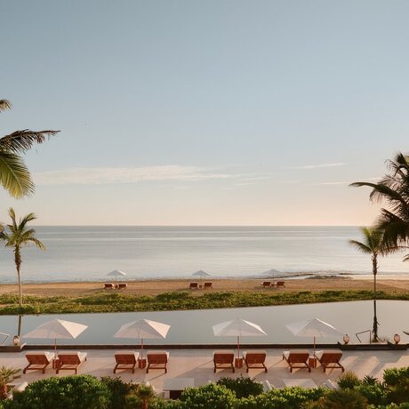 Amanvari's main pool overlooking the ocean at dawn, with palm trees and loungers on either side.