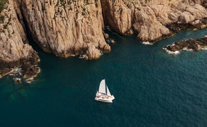 Aerial view of a catamaran sailing in turquoise waters near dramatic limestone cliffs at Amanoi, Vietnam.