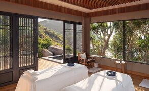 Double treatment room at Amanoi with spa bed, wooden screens, and views of surrounding greenery.