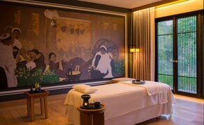 Amanoi spa treatment room with sunken bathtub, warm lighting, and Vietnamese artwork on ochre walls.